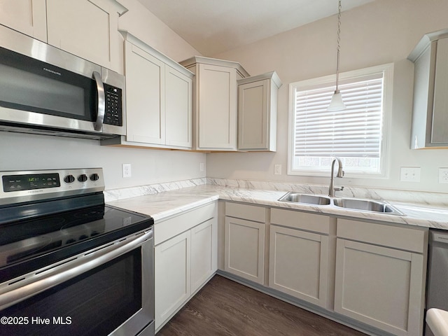 kitchen with dark wood-style floors, a sink, hanging light fixtures, light countertops, and appliances with stainless steel finishes