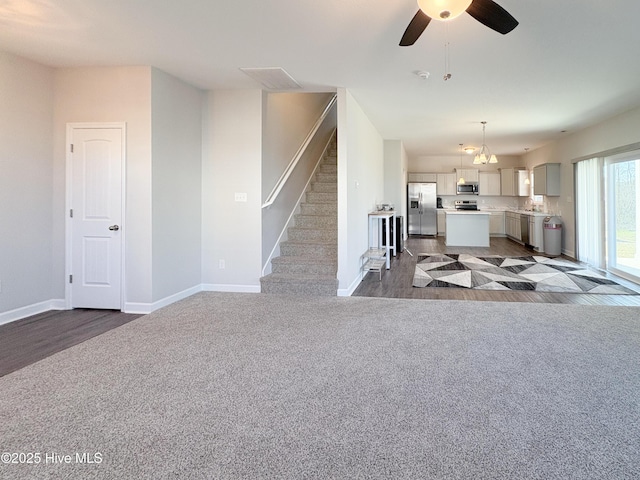 unfurnished living room with stairs, carpet, a ceiling fan, and baseboards