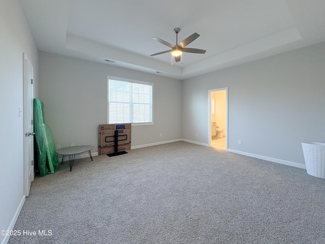 carpeted spare room with a tray ceiling, a ceiling fan, visible vents, and baseboards