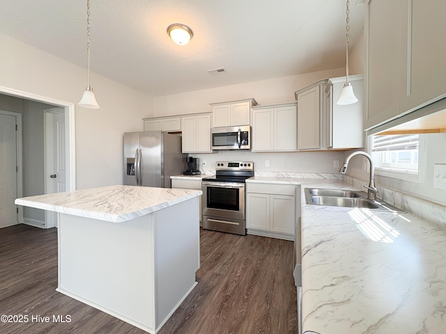 kitchen featuring a kitchen island, decorative light fixtures, appliances with stainless steel finishes, dark wood-style floors, and a sink