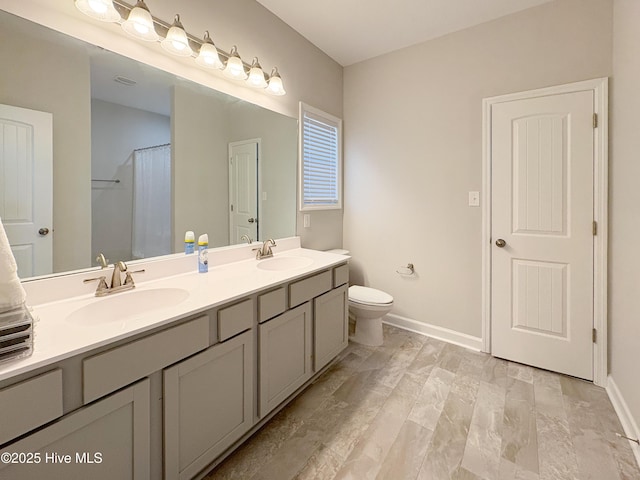 bathroom with a sink, baseboards, toilet, and double vanity