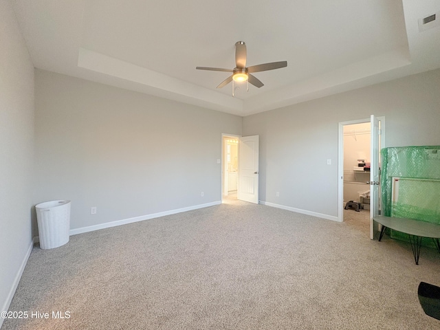 unfurnished bedroom with visible vents, a walk in closet, a raised ceiling, carpet floors, and baseboards