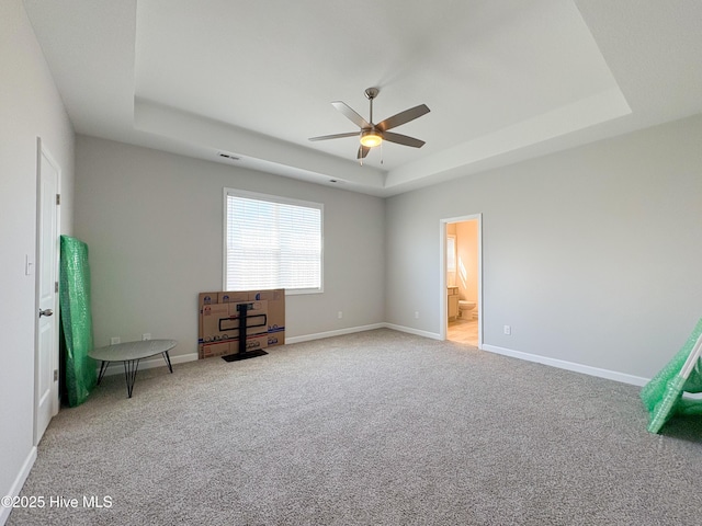 unfurnished bedroom featuring visible vents, baseboards, light colored carpet, ensuite bathroom, and a raised ceiling