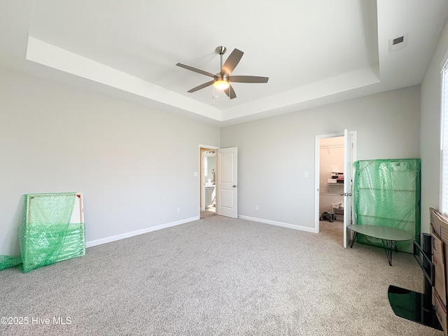 unfurnished bedroom with visible vents, a walk in closet, baseboards, a tray ceiling, and carpet flooring