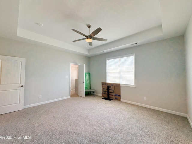 unfurnished bedroom featuring a tray ceiling, baseboards, visible vents, and light carpet