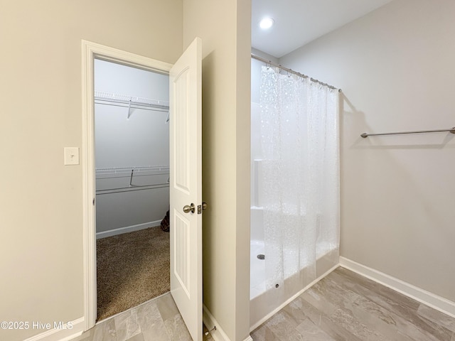 bathroom with a spacious closet, a shower with shower curtain, and baseboards