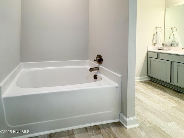 bathroom featuring vanity, a bath, wood finished floors, and baseboards