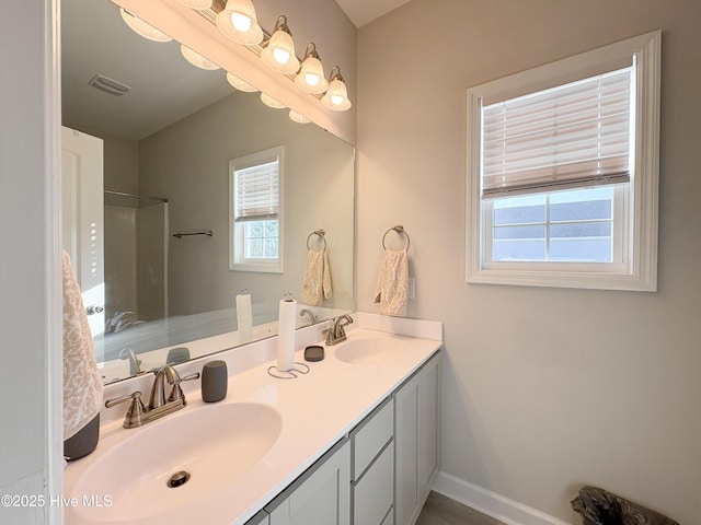 full bathroom with double vanity, a shower, baseboards, and a sink