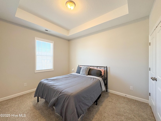 carpeted bedroom featuring a raised ceiling, baseboards, and visible vents