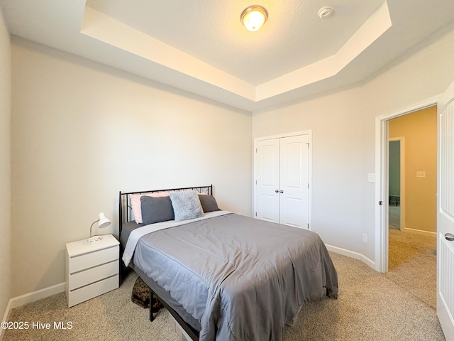 bedroom with a tray ceiling, baseboards, carpet floors, and a closet