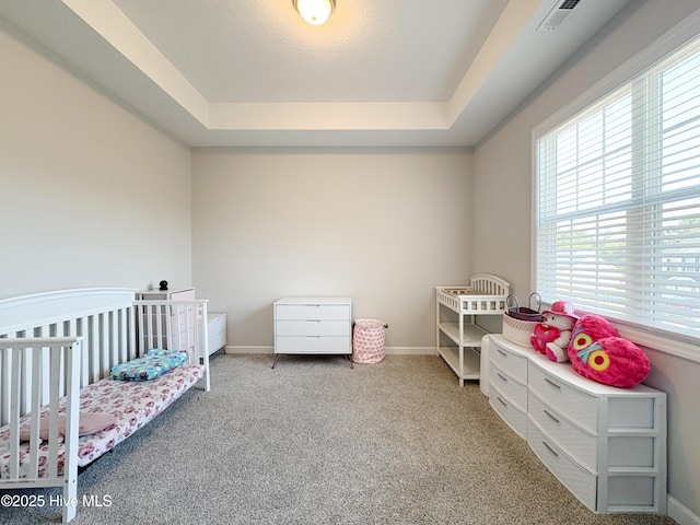 carpeted bedroom featuring visible vents, a crib, a raised ceiling, and baseboards