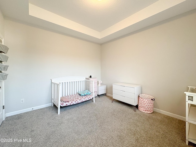 bedroom featuring baseboards, a raised ceiling, a crib, and carpet flooring