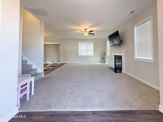 unfurnished living room with visible vents, baseboards, carpet, stairway, and a fireplace with flush hearth