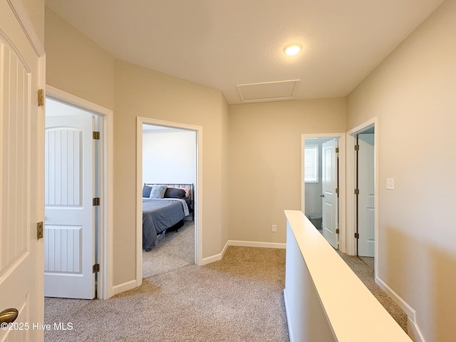 corridor featuring baseboards, an upstairs landing, light colored carpet, and attic access