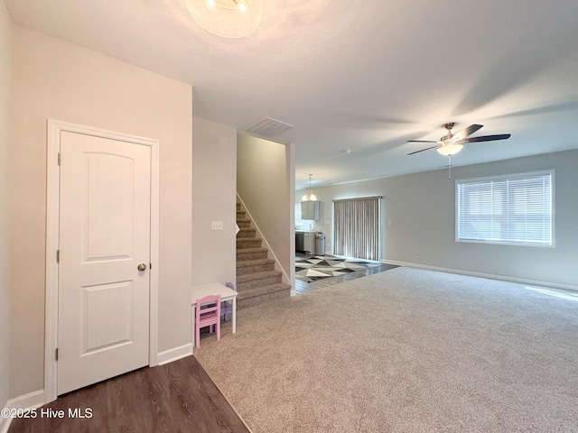 unfurnished room with a ceiling fan, baseboards, dark wood finished floors, stairs, and dark carpet