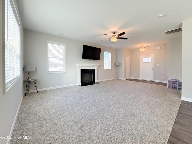 unfurnished living room with visible vents, a fireplace with flush hearth, a ceiling fan, carpet flooring, and baseboards