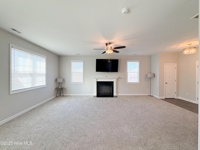 unfurnished living room featuring visible vents, a fireplace with flush hearth, carpet floors, and a healthy amount of sunlight