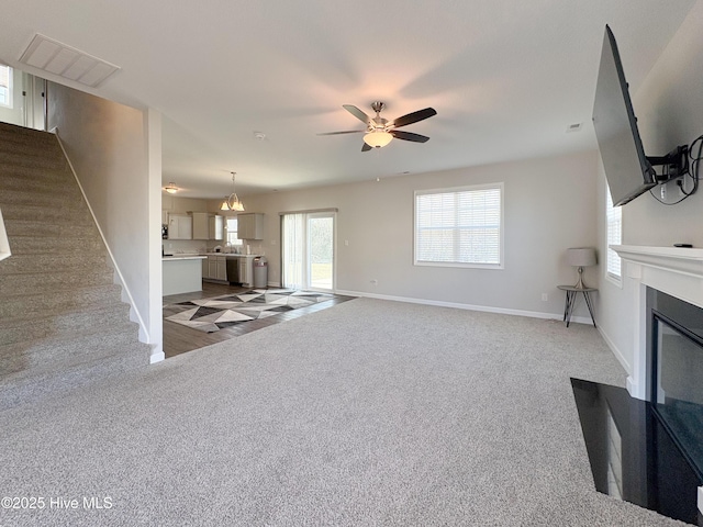 unfurnished living room featuring carpet, visible vents, a ceiling fan, stairs, and a glass covered fireplace