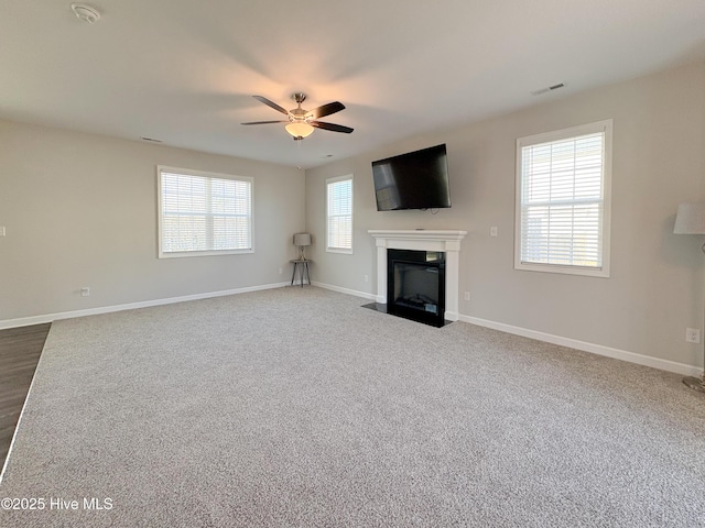 unfurnished living room with visible vents, baseboards, a fireplace with flush hearth, dark carpet, and a ceiling fan