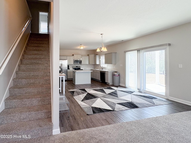 interior space with dark wood-type flooring, pendant lighting, a center island, stainless steel appliances, and light countertops