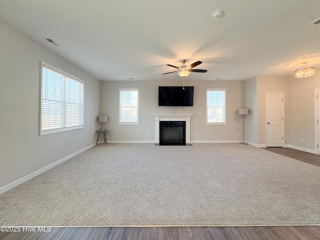 unfurnished living room featuring a ceiling fan, visible vents, carpet floors, baseboards, and a fireplace with flush hearth