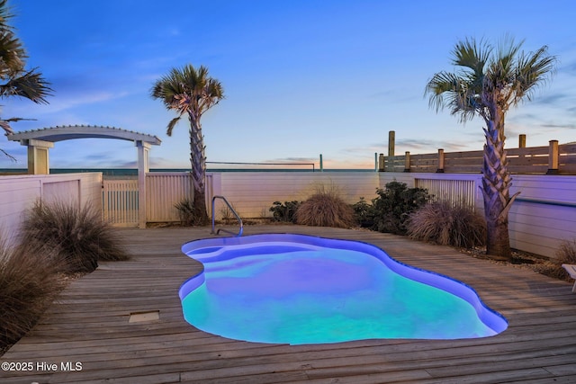 pool at dusk with fence, a deck, and a fenced in pool