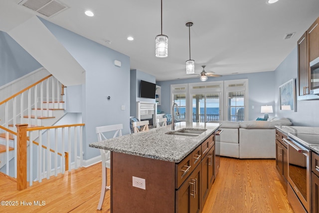 kitchen with a breakfast bar, a sink, visible vents, open floor plan, and stainless steel range with electric stovetop