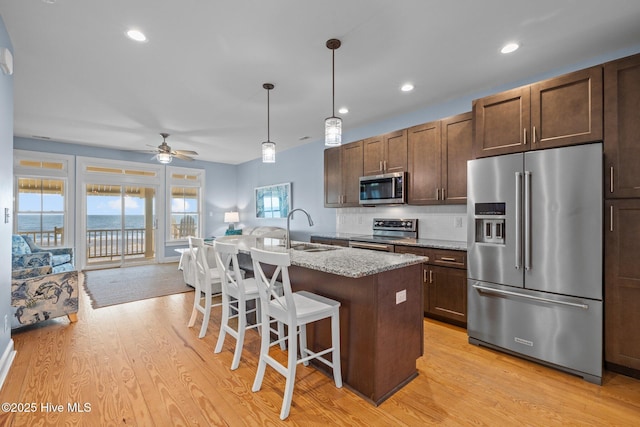 kitchen with light wood finished floors, decorative backsplash, an island with sink, appliances with stainless steel finishes, and a sink