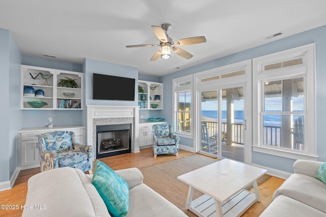 living room with visible vents, a fireplace, light wood-style flooring, and baseboards