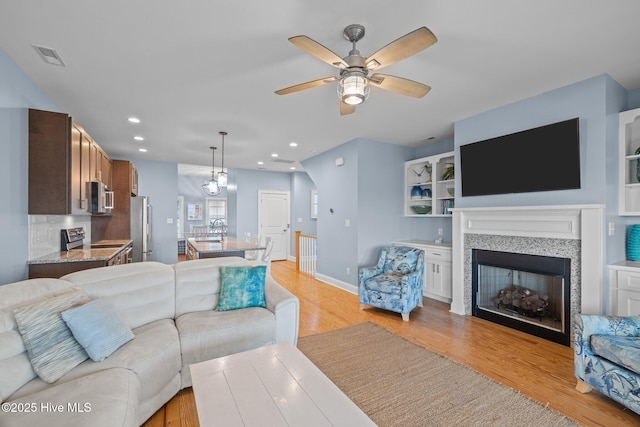 living area with baseboards, light wood-type flooring, a fireplace, and recessed lighting