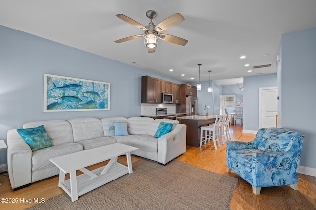 living room featuring light wood-style floors, ceiling fan, baseboards, and recessed lighting