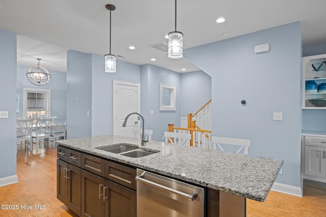 kitchen featuring light wood-type flooring, stainless steel dishwasher, a sink, and hanging light fixtures