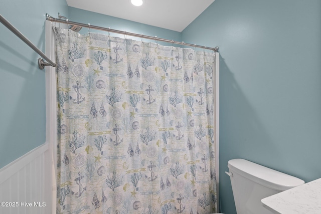 bathroom featuring toilet, a wainscoted wall, curtained shower, and a decorative wall