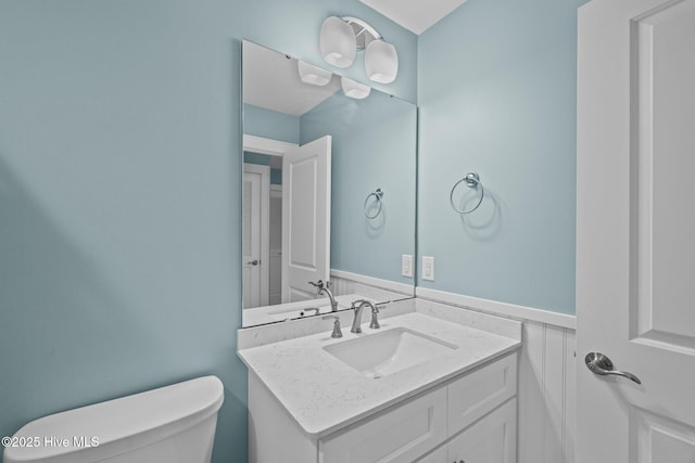 bathroom with a wainscoted wall, vanity, and toilet