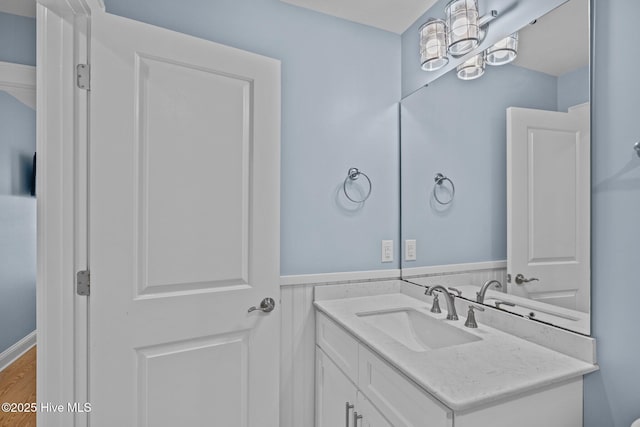 bathroom with a wainscoted wall, wood finished floors, vanity, and an inviting chandelier