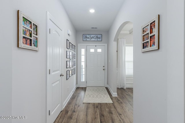 entrance foyer with arched walkways, dark wood-style flooring, visible vents, and baseboards