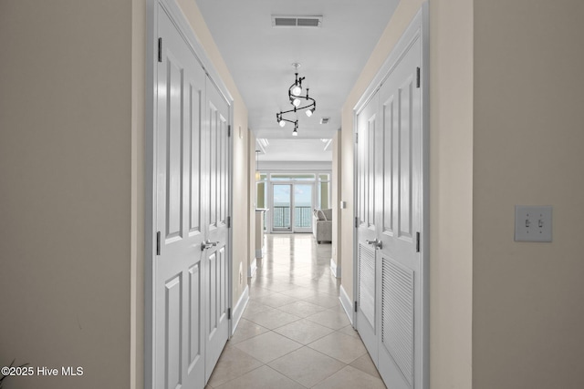 corridor featuring rail lighting, baseboards, visible vents, and light tile patterned flooring