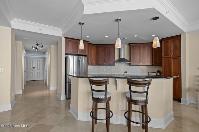 kitchen featuring wall chimney exhaust hood, a breakfast bar area, ornamental molding, freestanding refrigerator, and backsplash