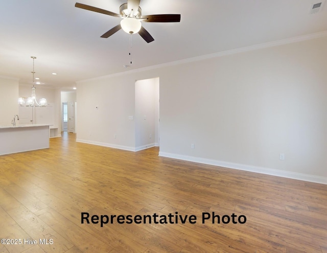 unfurnished living room with ceiling fan with notable chandelier, ornamental molding, light wood-type flooring, and baseboards