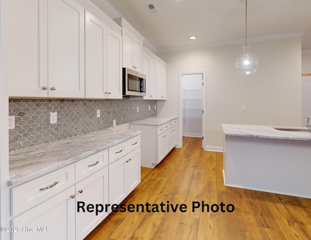 kitchen featuring white cabinets, stainless steel microwave, visible vents, and light stone countertops