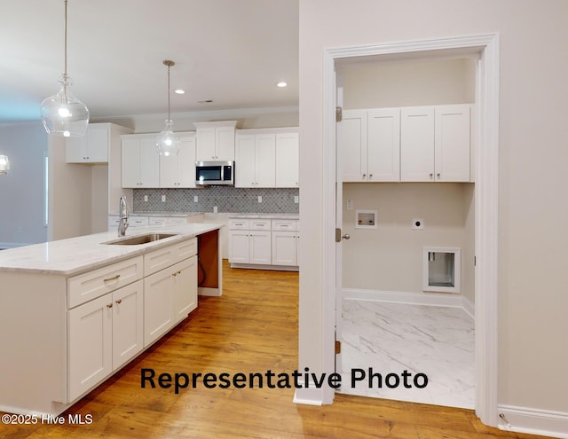 kitchen featuring tasteful backsplash, stainless steel microwave, ornamental molding, white cabinets, and a sink