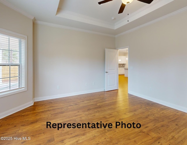 unfurnished room with ornamental molding, a tray ceiling, wood-type flooring, and baseboards