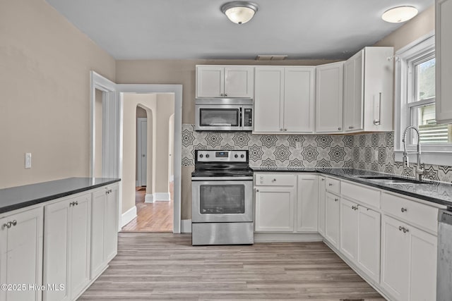 kitchen featuring arched walkways, stainless steel appliances, visible vents, backsplash, and a sink