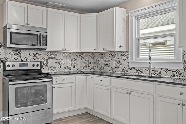 kitchen featuring appliances with stainless steel finishes, dark countertops, white cabinetry, and a sink