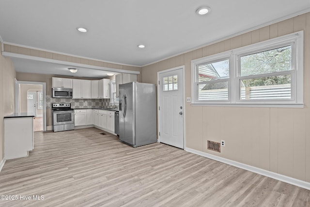 kitchen with crown molding, dark countertops, visible vents, appliances with stainless steel finishes, and light wood-style floors