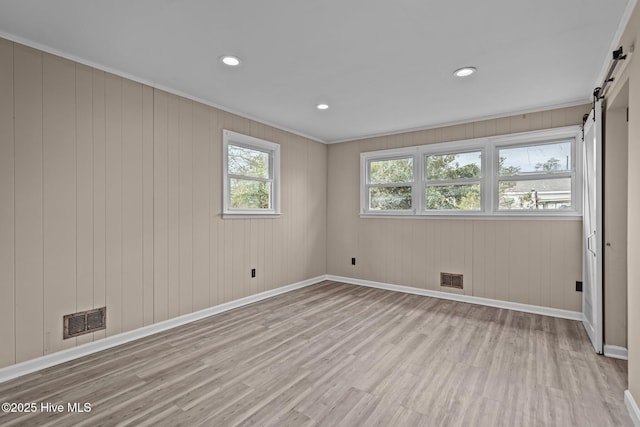 spare room featuring wood finished floors, visible vents, baseboards, and a barn door