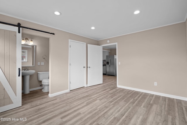 unfurnished bedroom with light wood-style floors, a barn door, ornamental molding, and stainless steel refrigerator with ice dispenser