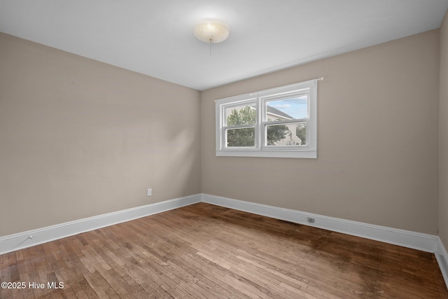 empty room with hardwood / wood-style floors, visible vents, and baseboards