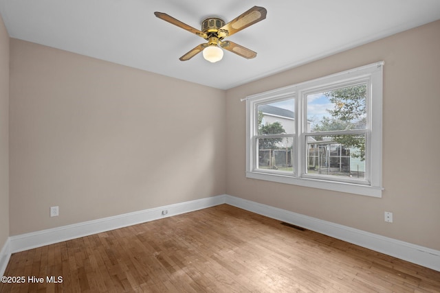 empty room featuring a ceiling fan, visible vents, baseboards, and wood finished floors