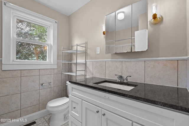 bathroom with toilet, a wainscoted wall, vanity, and tile walls